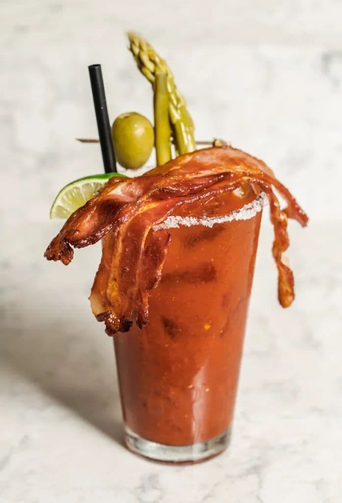 A Bloody Mary garnished with strips of bacon, olives, asparagus and lime.