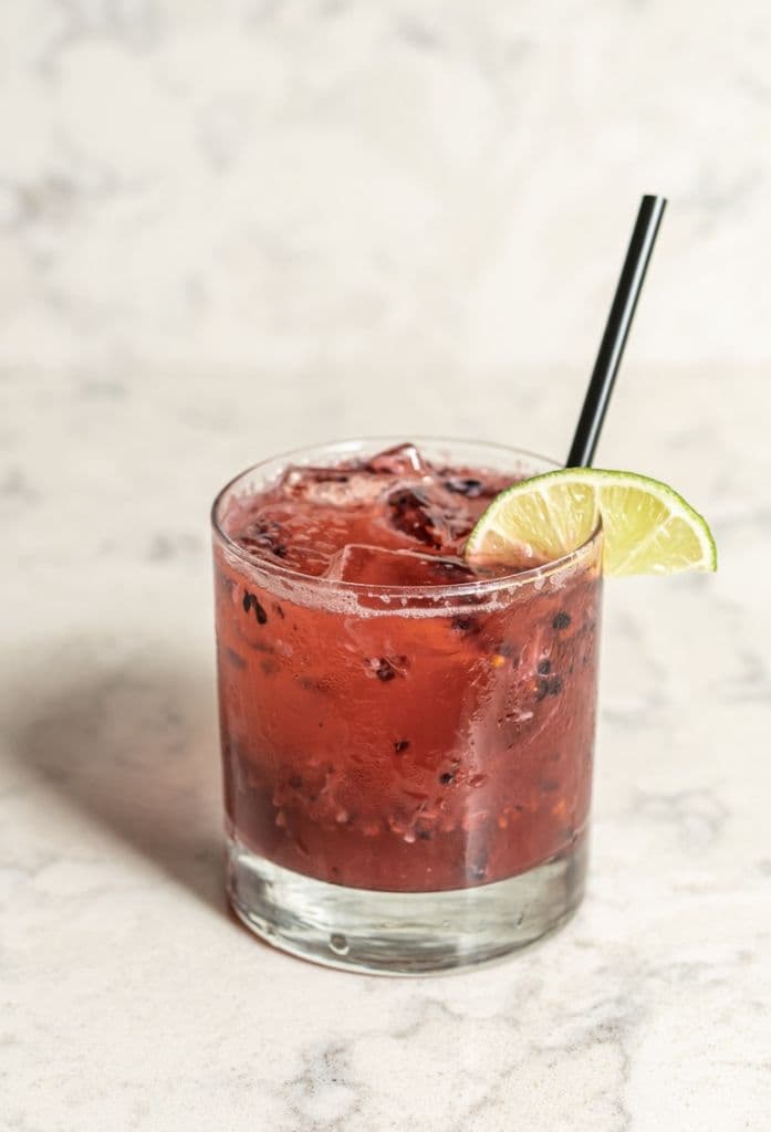 A deep red berry cocktail over ice with a lime wheel.