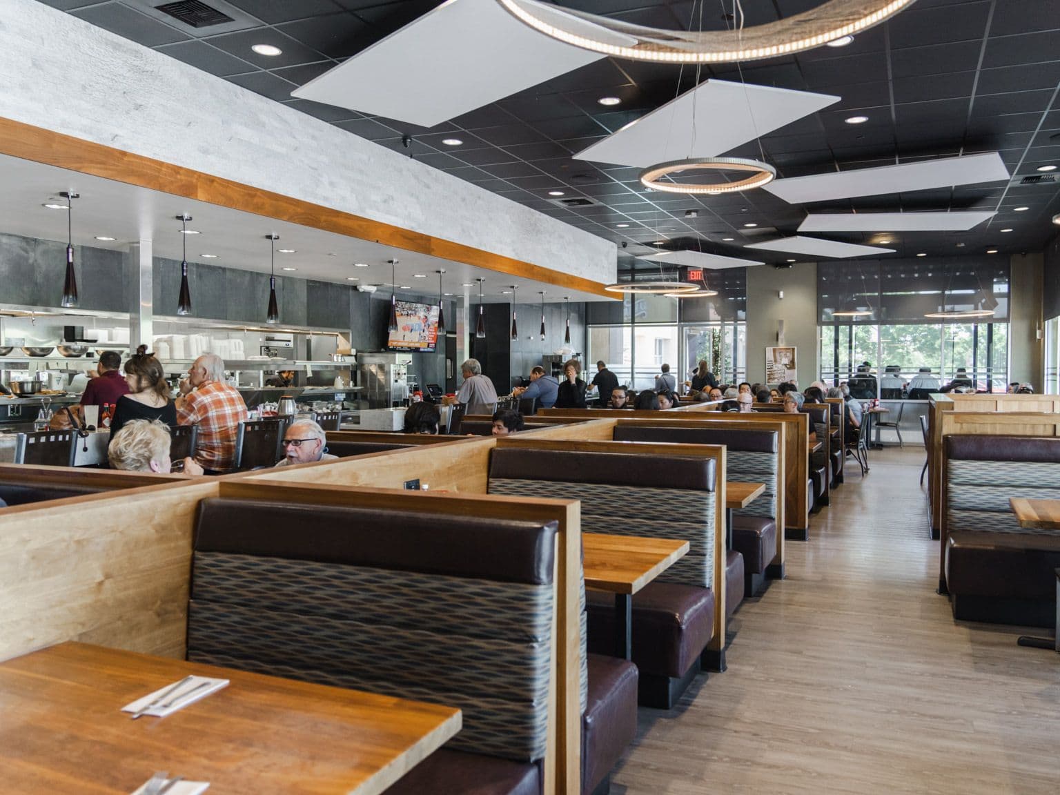 The dining room: rows of booths with dark leather seats and wood tables, guests eating, and the open kitchen counter at the back.