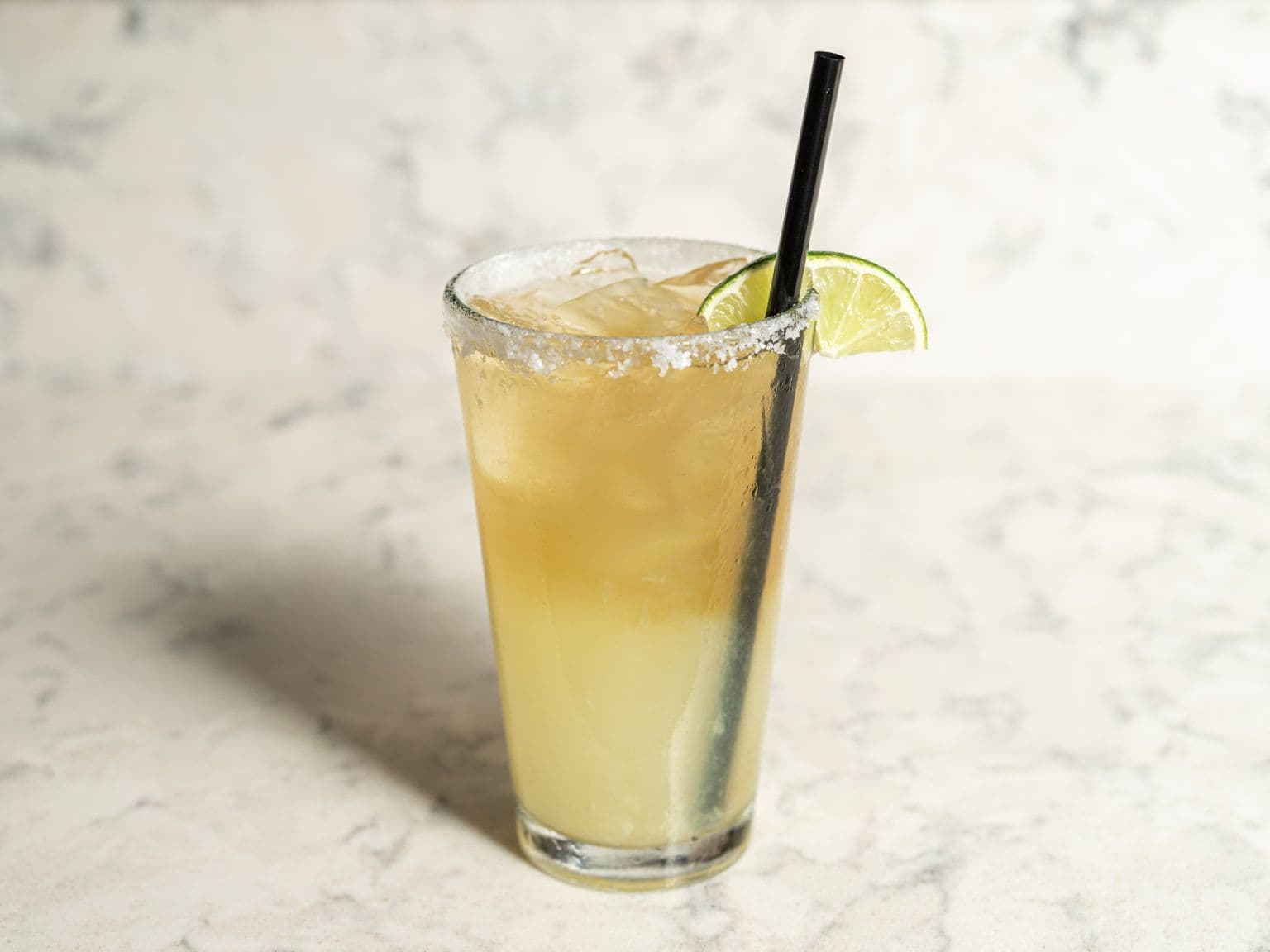 A salt-rimmed citrus cocktail over ice with a lime wedge.