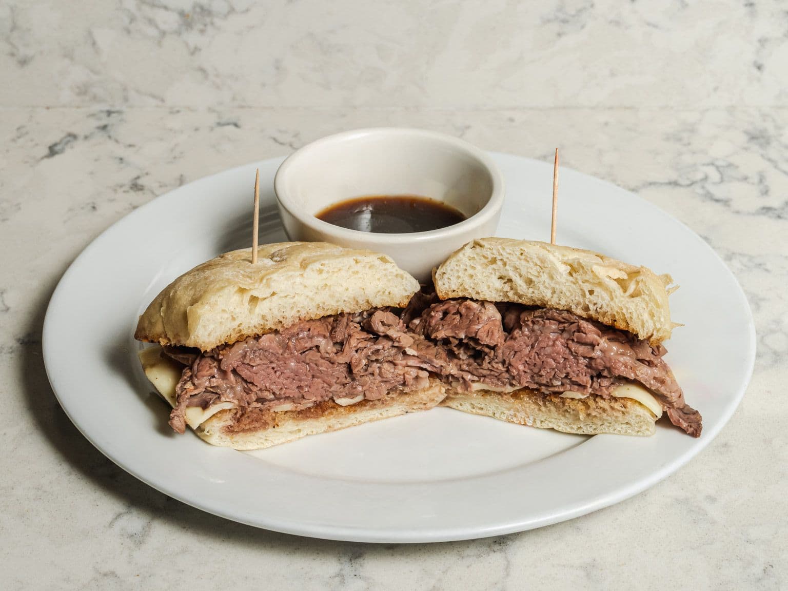 Prime rib dip sandwich on a ciabatta roll, cut in half, with a cup of au jus.