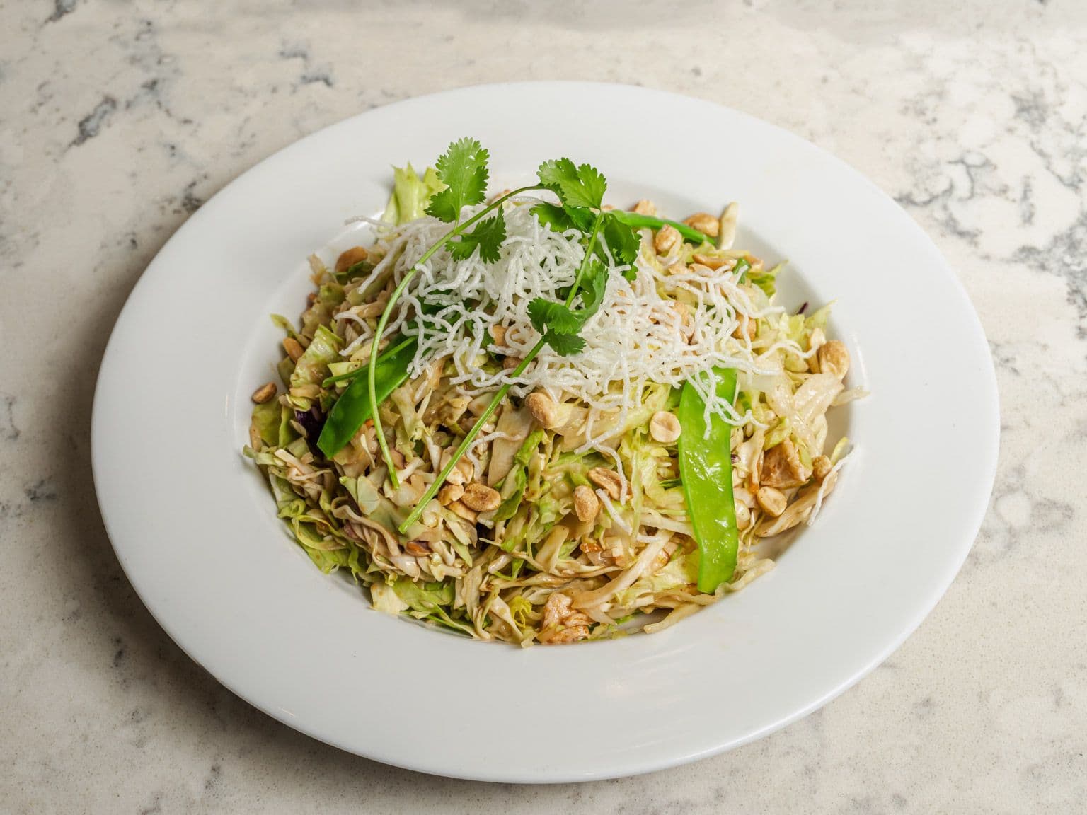A chicken salad with shredded cabbage, crispy rice noodles, snow peas and cilantro.