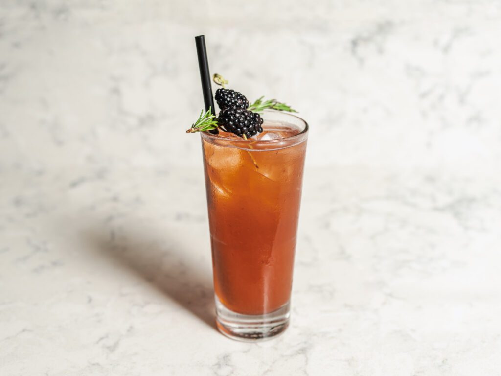 dark cocktail with raspberries on rim and straw in tall glass